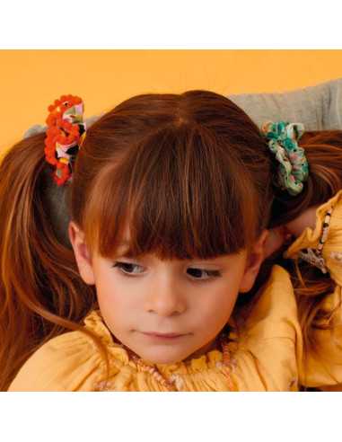 Criança com cabelo comprido, usando dois chouchous Djeco (um verde e um laranja) para prender duas tranças laterais.