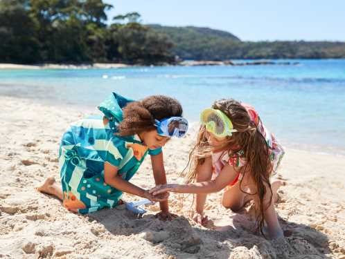 Criança (3-5 anos) a usar o poncho toalha Dock and Bay azul-escuro com padrão de ondas, ideal para praia ou piscina, mostrando a secagem rápida.