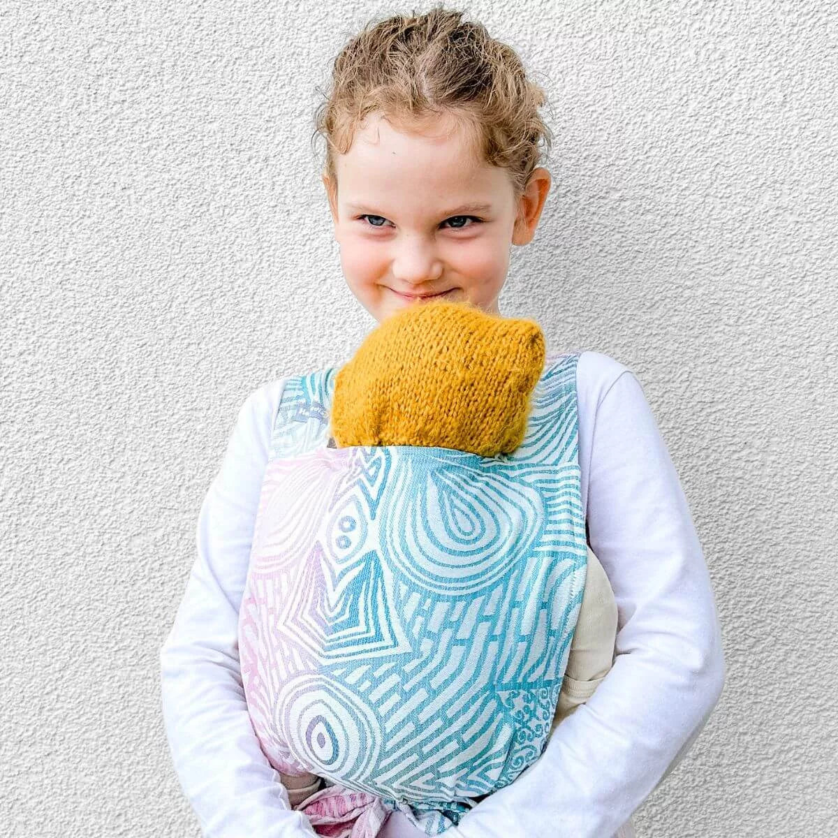 Criança a utilizar o porta-bebé de bonecas Hoppediz Jaipur Cream para carregar um boneco de forma ergonómica.