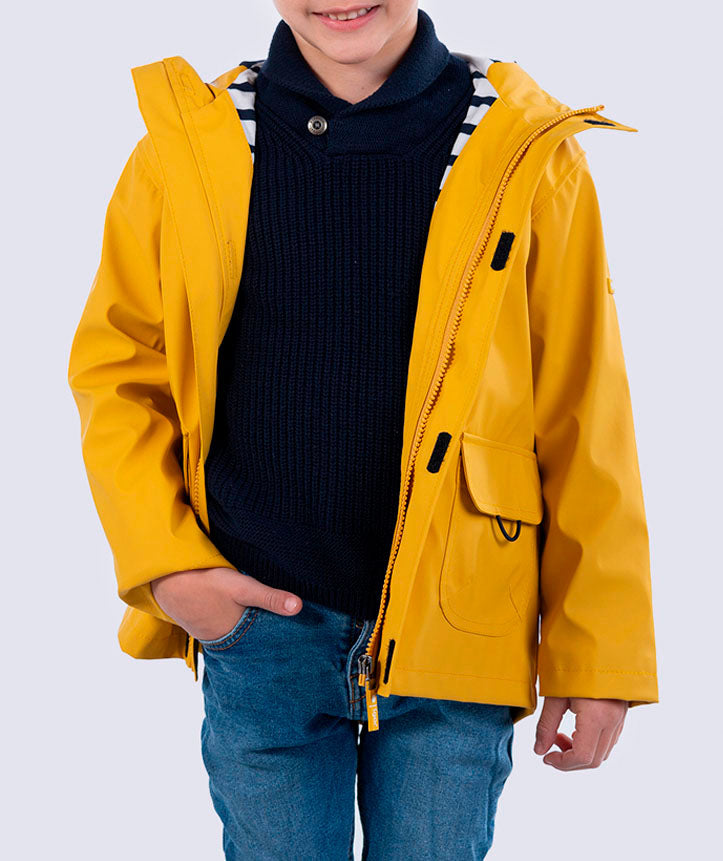 Criança a vestir o casaco impermeável amarelo Igor, aberto sobre um camisola azul escura e calças de ganga, com a mão no bolso.