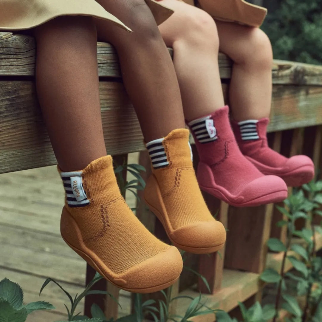 Crianças sentadas com as pernas penduradas, usando diferentes cores dos Attipas Rain Boots, mostrando o design flexível e prático.