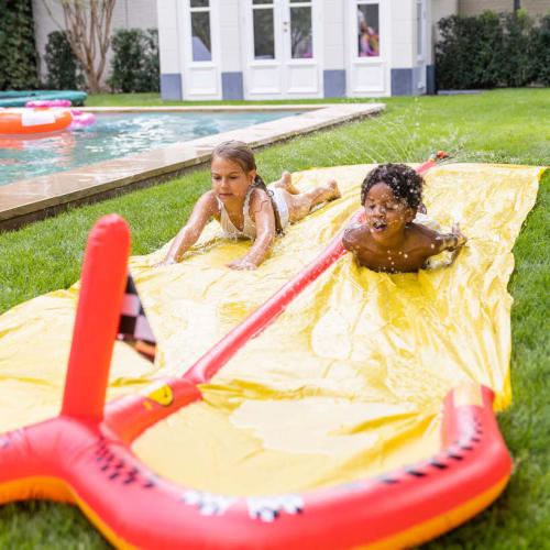 Crianças a deslizar no escorrega duplo de água insuflável, diversão ao ar livre em dia de verão, momentos de alegria e refrescância em família.