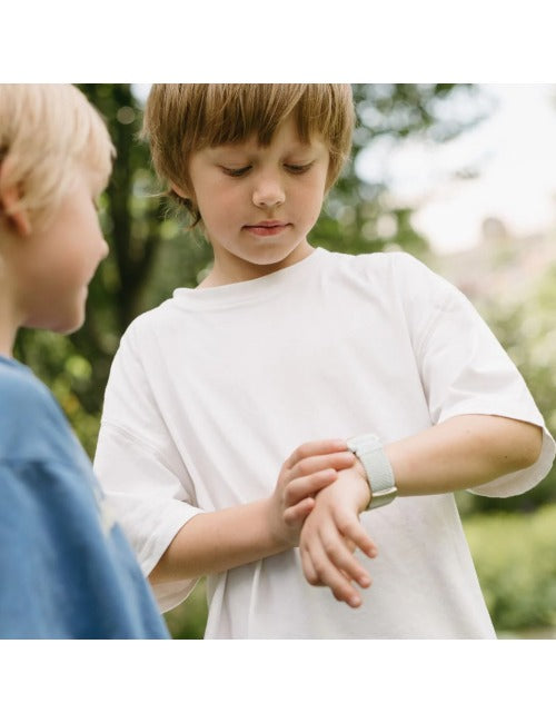 Duas crianças no exterior, uma a olhar para o relógio KidyWolf K-watch que a outra criança tem no pulso, ambas com roupa casual.
