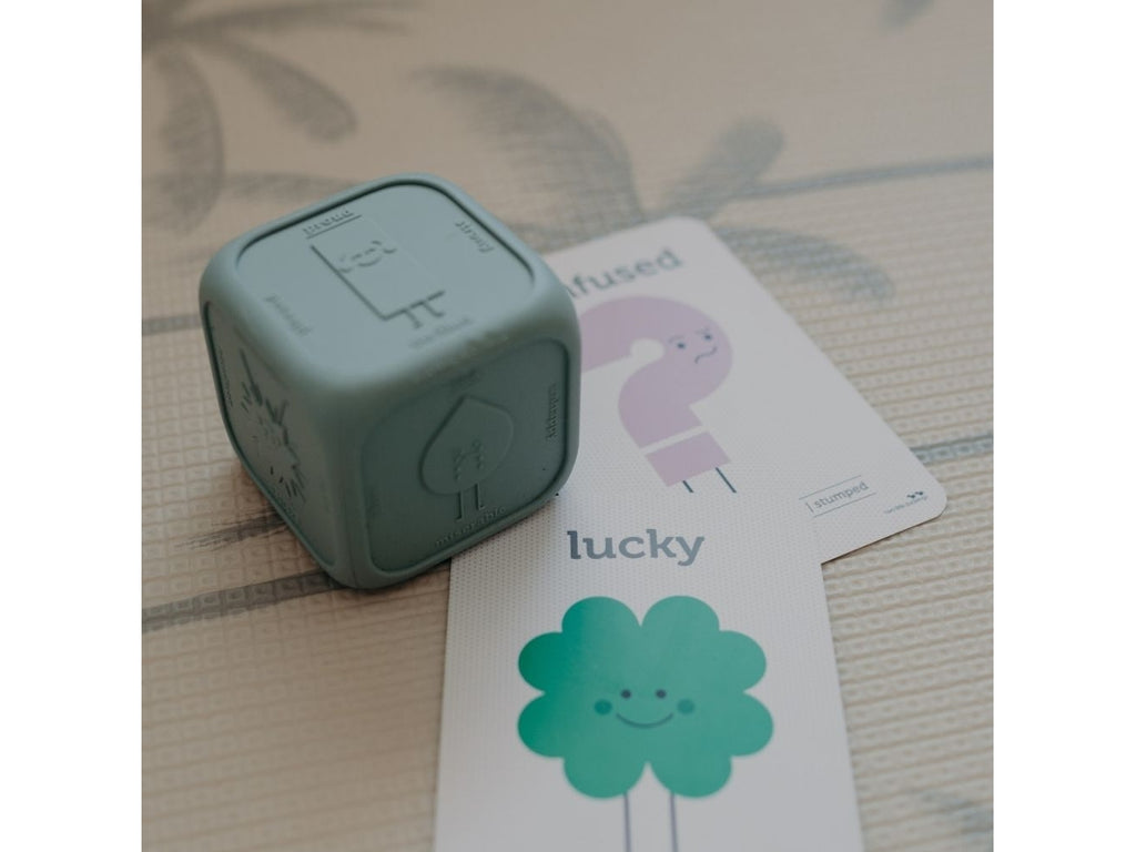 Cubo de silicone ao lado de cartões ilustrados com emoções, um deles mostrando um trevo verde para 'lucky'.