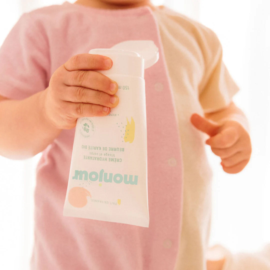 Pormenor das mãos de uma criança pequena a manusear a embalagem do creme Monjour.