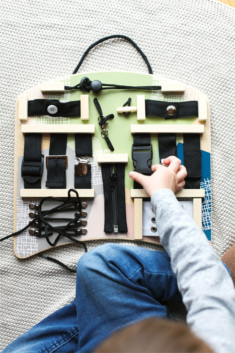 Detalhe do quadro de atividades mostrando a variedade de fechos e mecanismos disponíveis para a criança explorar.