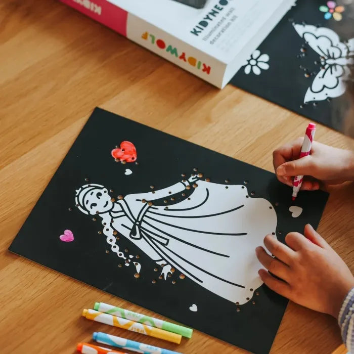 Detalhe das mãos de uma criança a marcar uma placa de desenho de uma princesa para o kit neon.