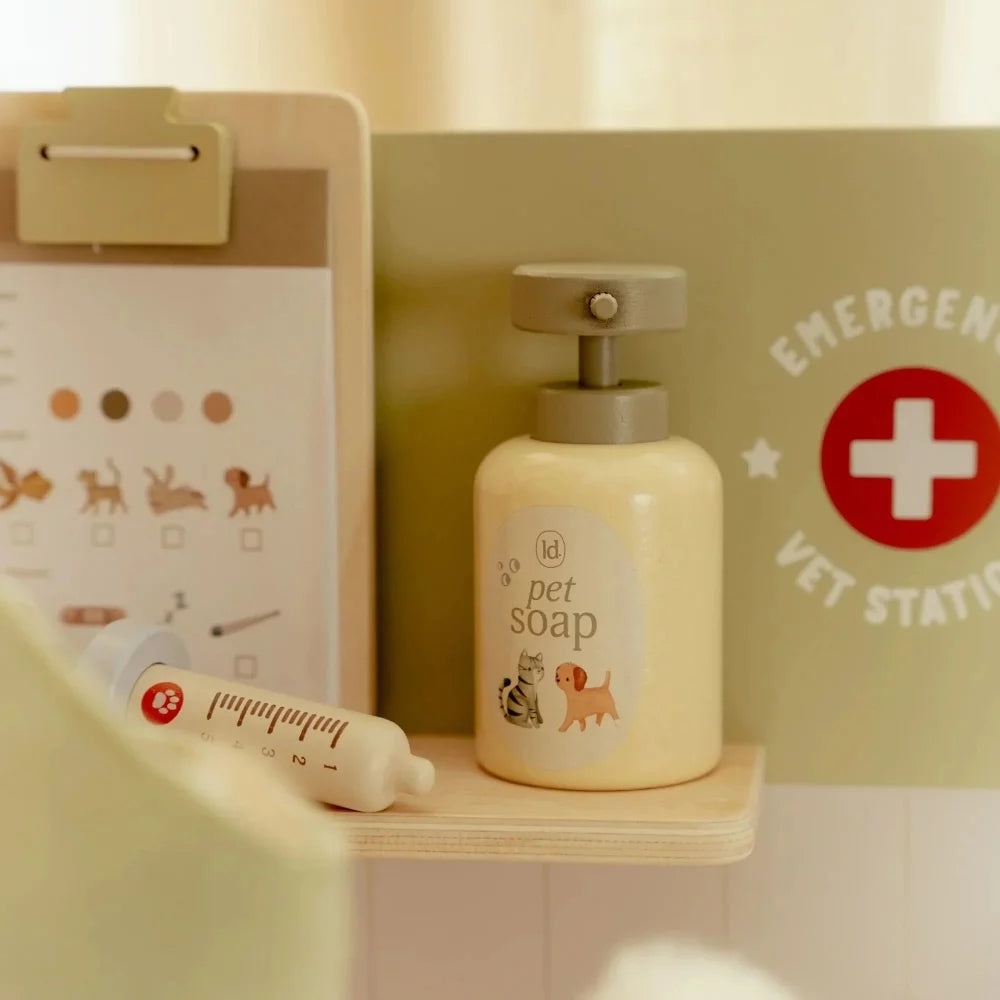 Detalhe da seringa e do frasco de sabão para pets na prateleira da clínica, com o fundo verde da estação de emergência visível.