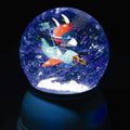 Globo de neve Djeco aceso, mostrando um avião com um piloto animal a voar entre flocos brilhantes sobre uma base azul escura.