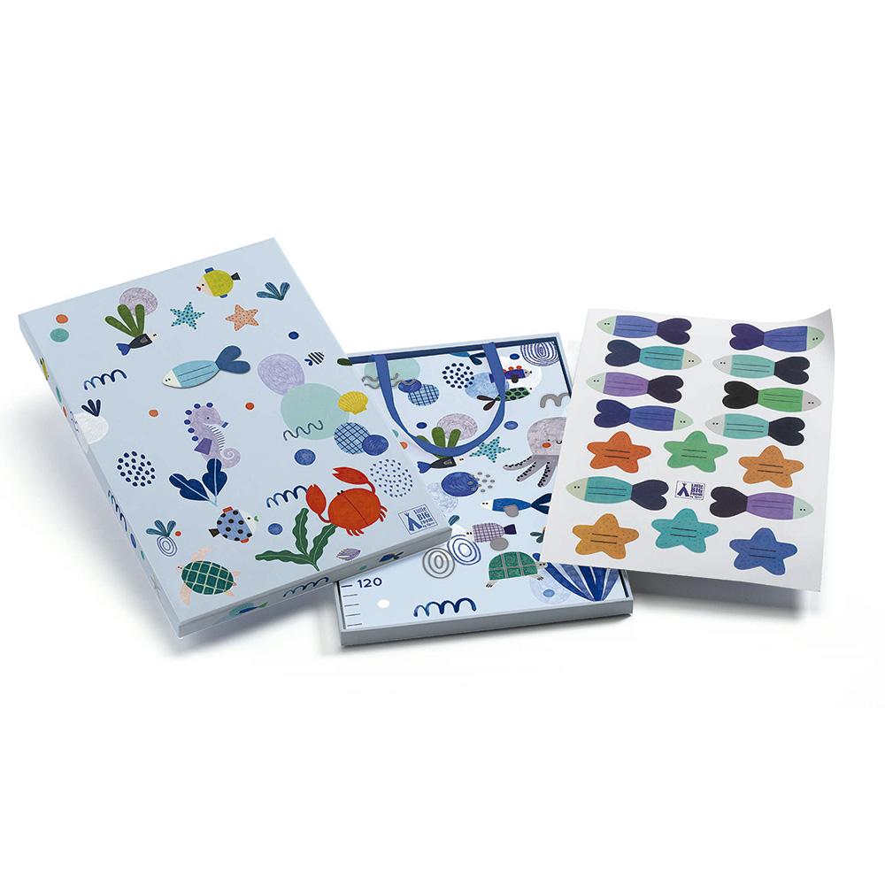 Conjunto completo da tabela de altura Djeco: caixa de arrumação, tabela dobrada e folha de autocolantes reposicionáveis em forma de peixes e estrelas.