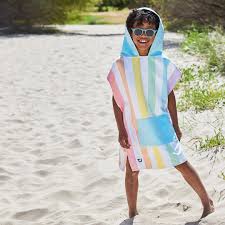 Criança sorridente na praia, vestindo o poncho de microfibra Dock and Bay com riscas coloridas, ideal para secagem rápida após o banho de mar.