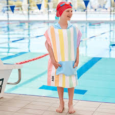 Menino com touca de natação sorri junto à piscina, vestindo o poncho de praia Dock and Bay com bolso frontal em rede.