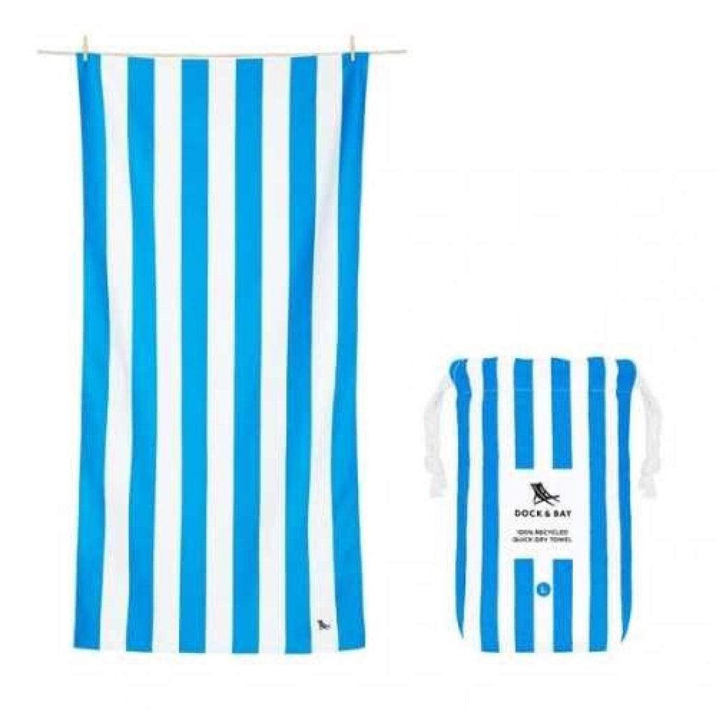 Toalha de praia Dock and Bay azul e branca de riscas verticais ao lado da sua bolsa de transporte compacta com o mesmo padrão.