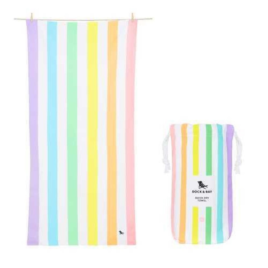 Toalha de praia Dock and Bay de secagem rápida com riscas verticais em cores pastel (lilás, azul, amarelo, verde, rosa) e bolsa de transporte a condizer, suspensas.