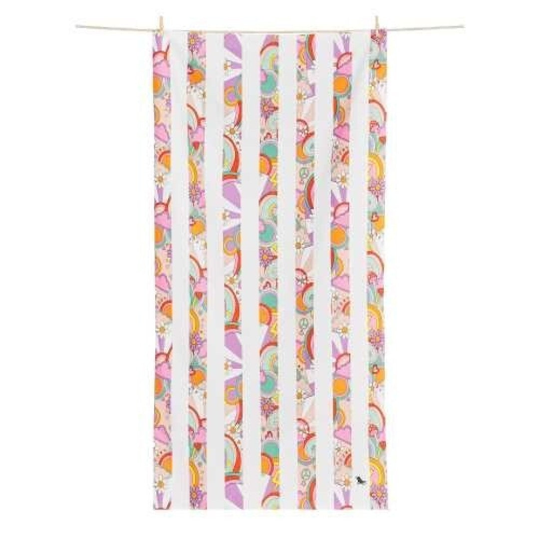 Toalha de praia Dock and Bay com riscas brancas e padrão psicadélico colorido (arcos-íris, flores, símbolos da paz) em algumas riscas, suspensa num varal.