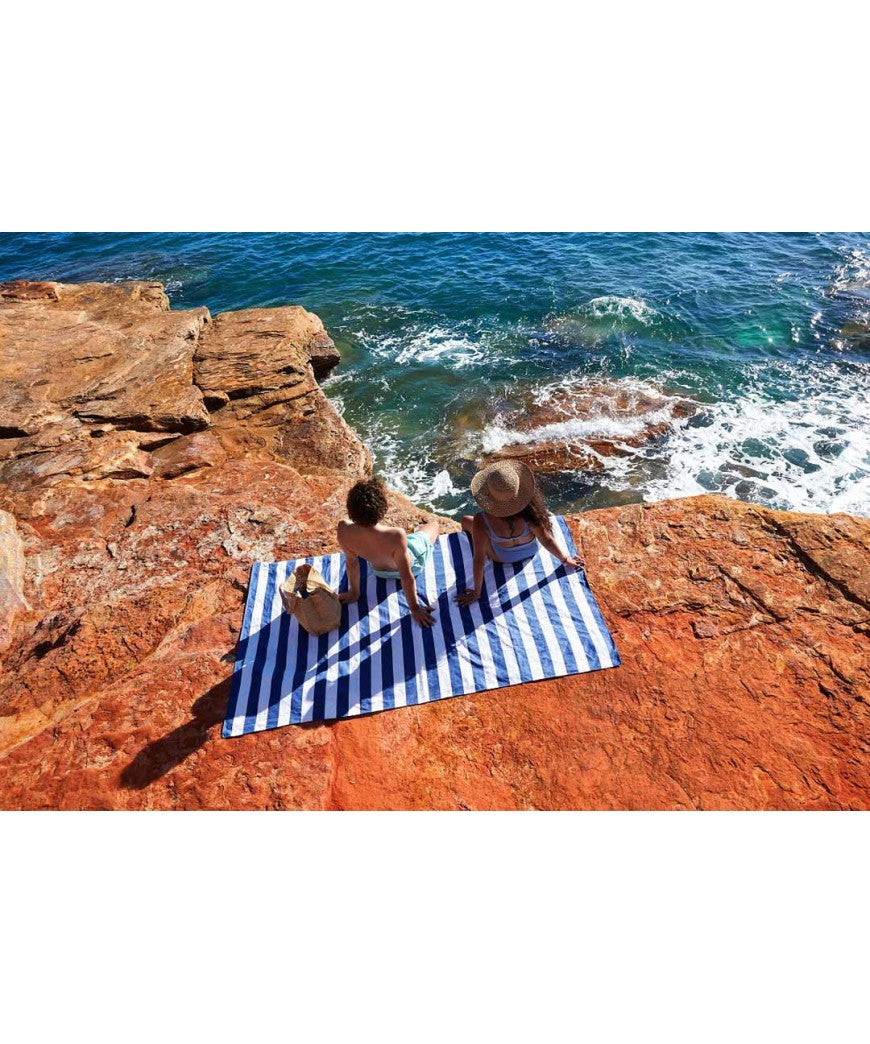 Detalhe da manta de piquenique Dock & Bay dobrada e compacta dentro da sua bolsa de transporte azul, pronta para levar.