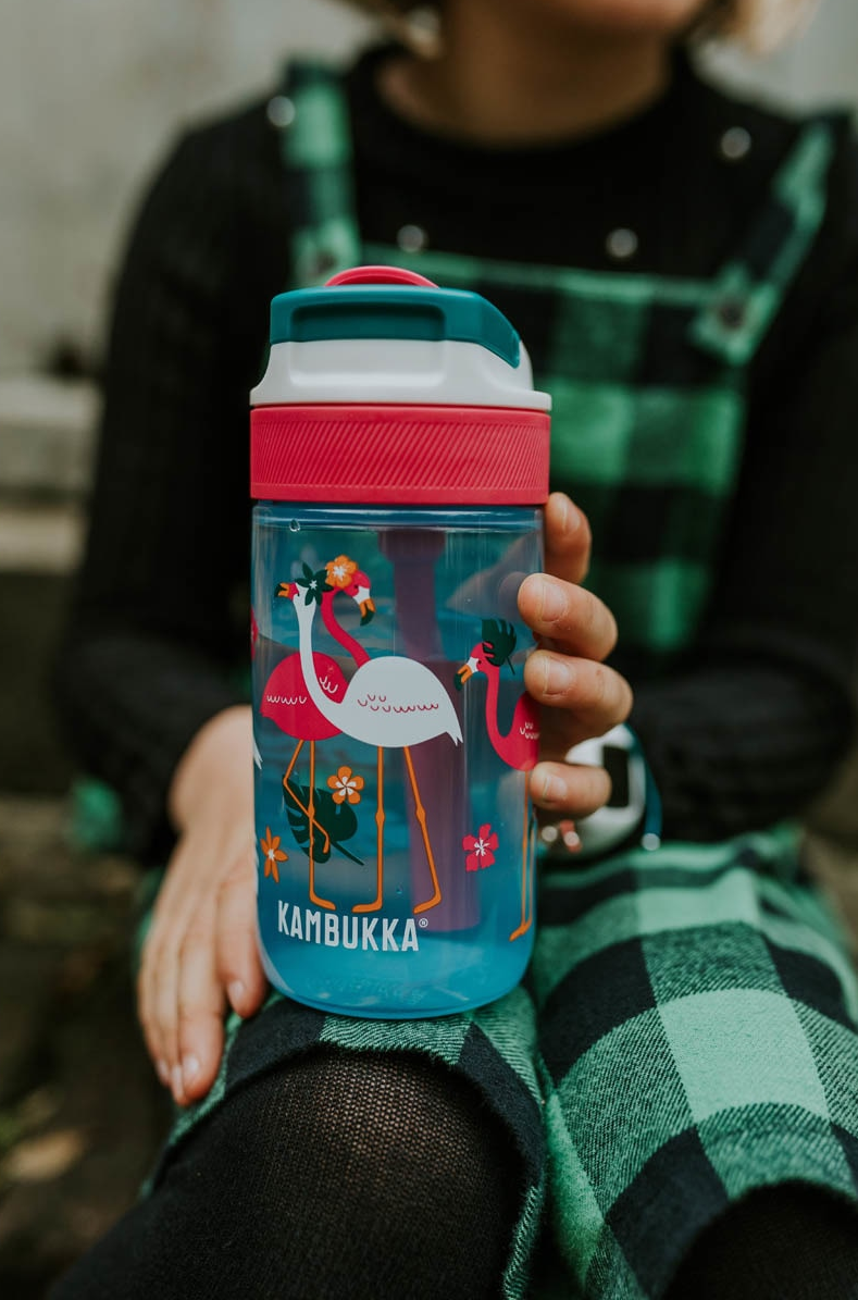 Criança segura a garrafa Kambukka LAGOON Blue Flamingo 400ml, exibindo o design vibrante com flamingos.