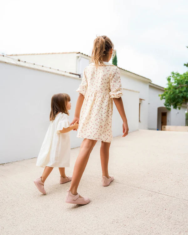 Duas crianças a caminhar de mãos dadas, ambas a usar calçado barefoot rosa.