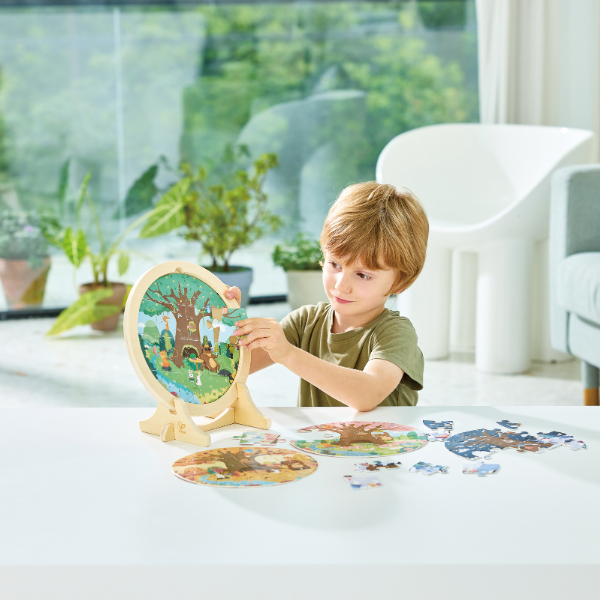 Criança a montar o puzzle de outono do Hape 4 Estações 4 Puzzles no suporte de madeira, com outras peças na mesa.