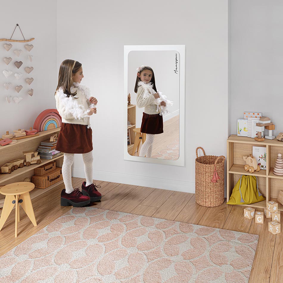 Menina a usar o espelho Micuna Micurssori na posição vertical como espelho de corpo inteiro no quarto.