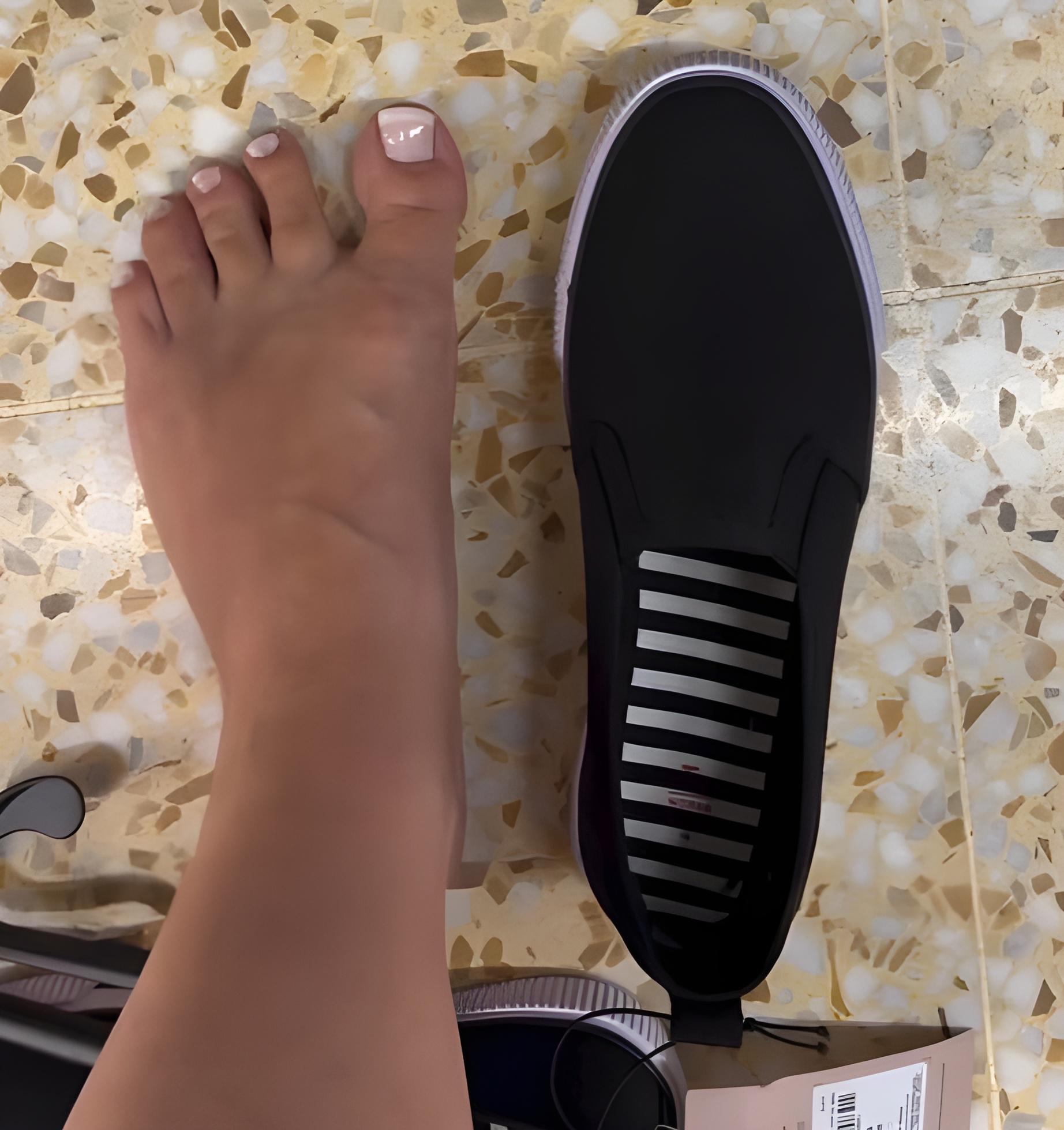 Pé descalço ao lado de um sapato preto de sola branca, ilustrando a comparação de tamanho no contexto do evento Barefoot.