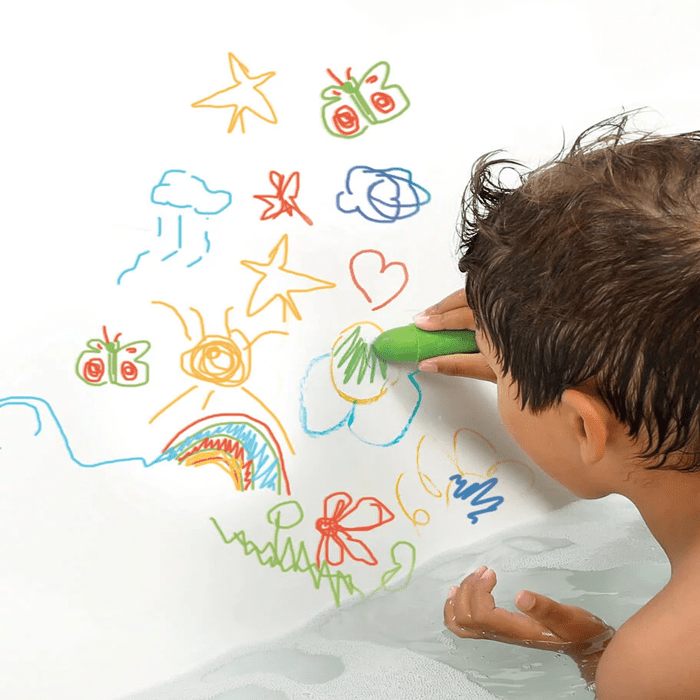 Criança a desenhar ativamente na parede da banheira com um lápis verde Ludi, rodeada por desenhos coloridos.
