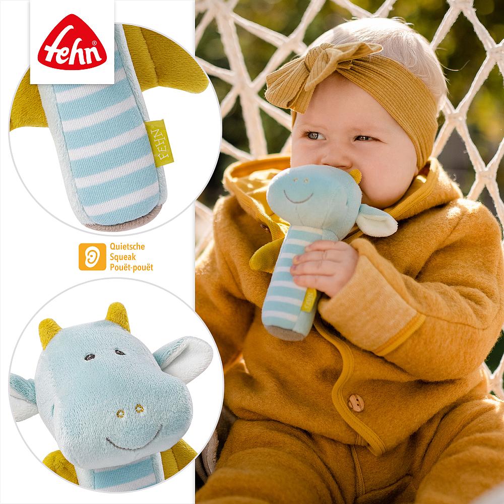 Bebé a segurar e a levar à boca o Guizo Dragão Fehn, com detalhes ampliados do brinquedo e o ícone de guincho.