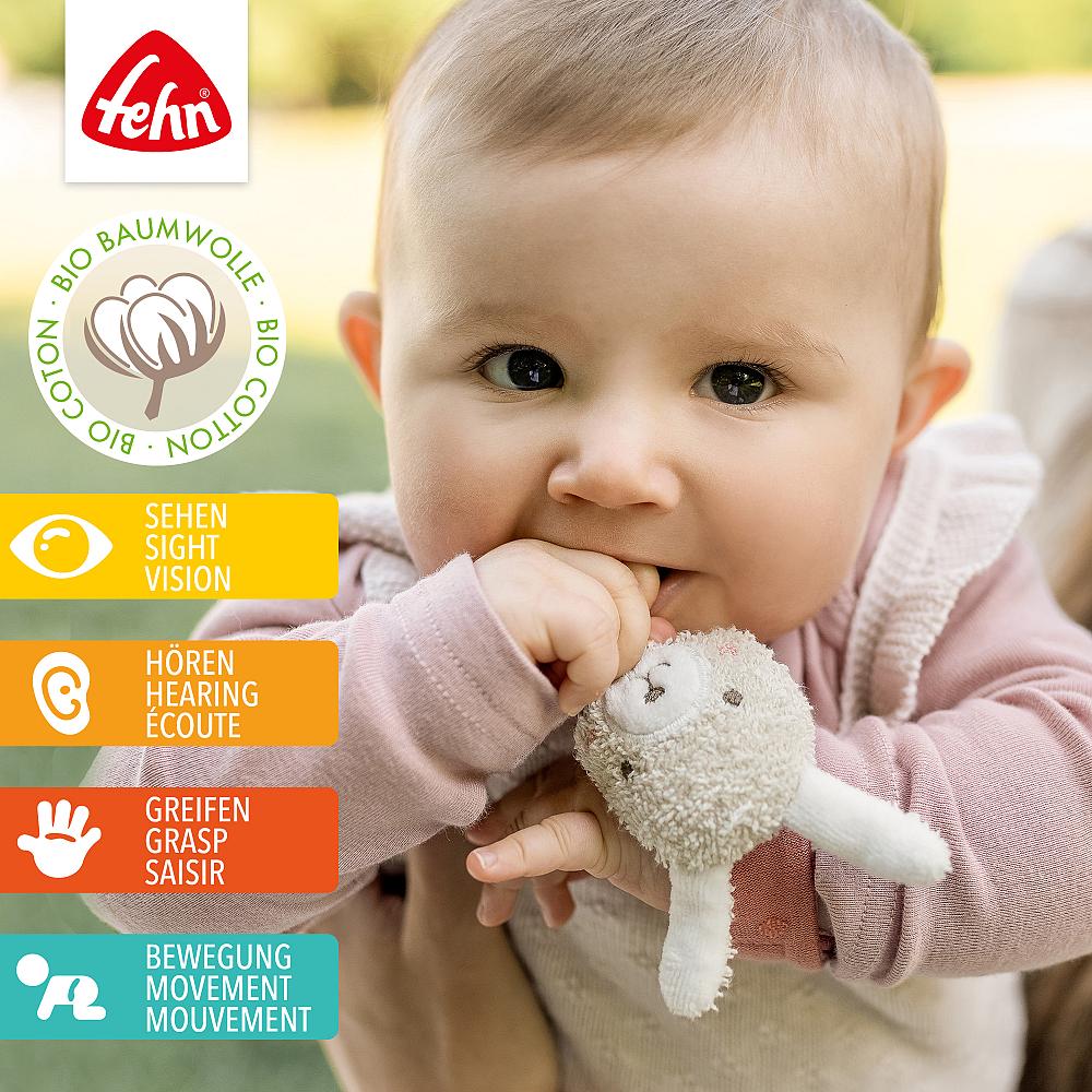 Bebé a morder a pulseira de atividades Fehn com guizo coelho, destacando os benefícios para visão, audição, preensão e movimento (0+ meses).