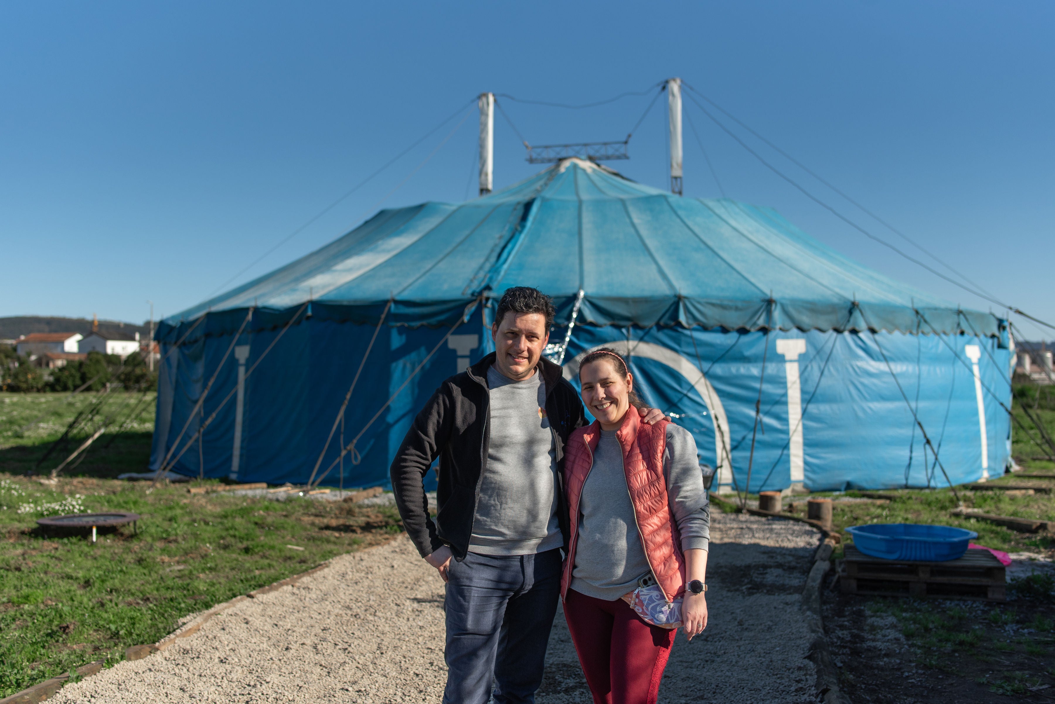 Dois anfitriões sorridentes da Aldeia Gotu em frente à Tenda Azul, prontos para celebrar festas de aniversário.