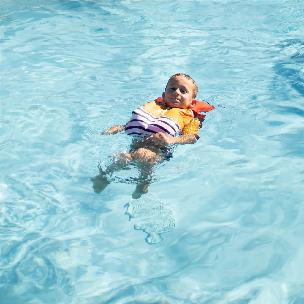 Criança pequena flutuando de costas na água de uma piscina, usando a T-shirt Floatee com colete salva-vidas insuflado para segurança.