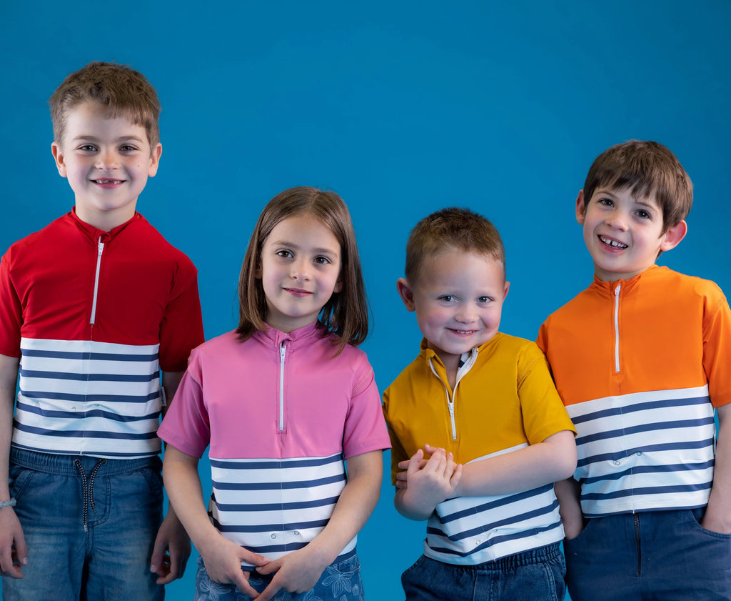 Quatro crianças sorridentes vestindo T-shirts de natação Floatee com riscas e cores vibrantes (vermelho, rosa, amarelo, laranja) sobre fundo azul.