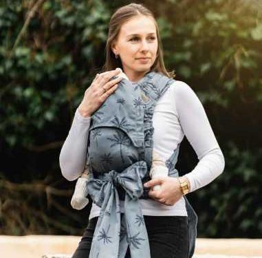 Mulher sorridente com um porta-bebés azul com padrão amarrado na frente.