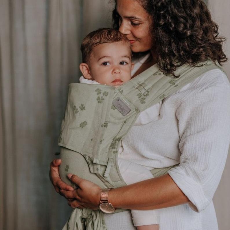 Mulher abraçando um bebé que está no Mei Tai Fidella FlyClick Toddler Clover verde claro, em posição frontal.