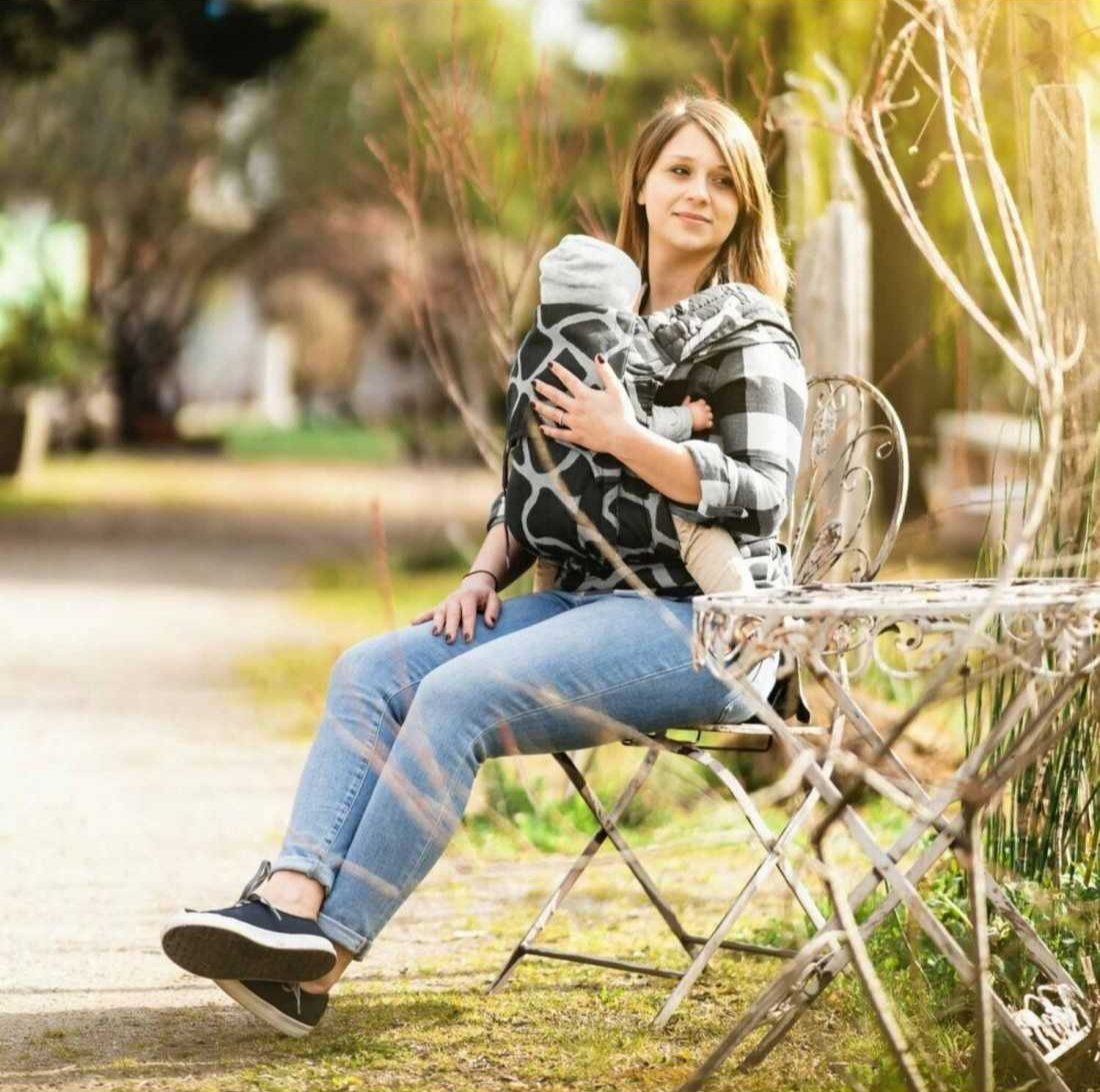 Mulher sentada ao ar livre usando o porta-bebé Fidella® Fly Tai, exibindo a praticidade em ambientes externos.