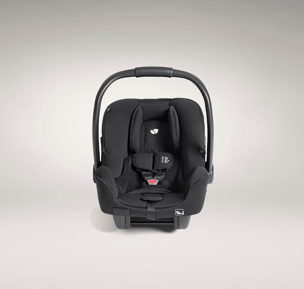Vista frontal detalhada da cadeira auto ovo Joie i-Starter preta, focando no apoio de cabeça com o logótipo bordado da folha no centro.