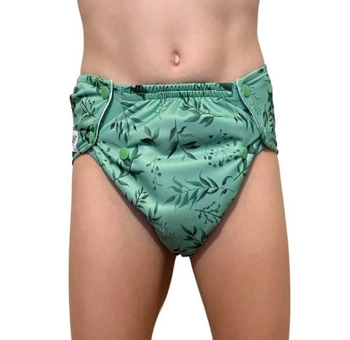 Criança a vestir a fralda reutilizável Pupus Feel Green com padrão de folhas verdes e ajuste de molas.