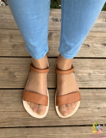 Vista superior de pés calçados com as sandálias Froddo cor de conhaque sobre um pavimento de madeira.