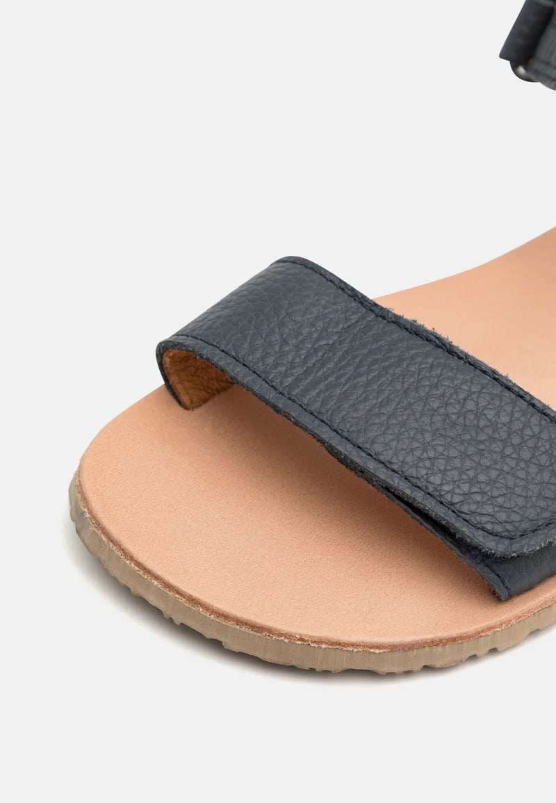 Detalhe da textura da pele lisa azul escura e da tira de velcro da sandália minimalista Froddo Flexy Lia.