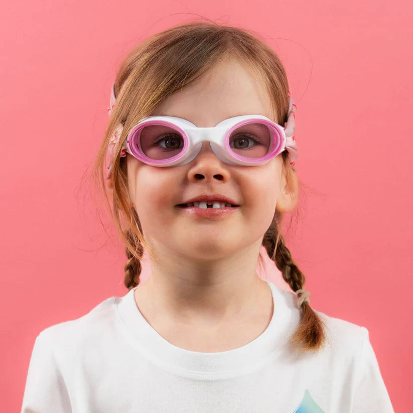 Menina com um sorriso doce a usar os óculos Waterplops Cerejas, com foco nas lentes cor-de-rosa e na banda com padrão de cerejas, contra um fundo rosa vibrante.