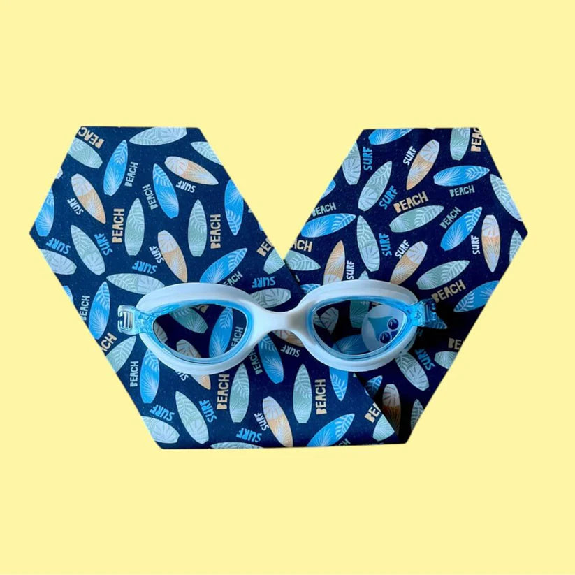 Waterplops Óculos para Piscina Surf em armação branca e lentes azuis, sobre uma superfície hexagonal com o padrão de pranchas de surf, em fundo amarelo.