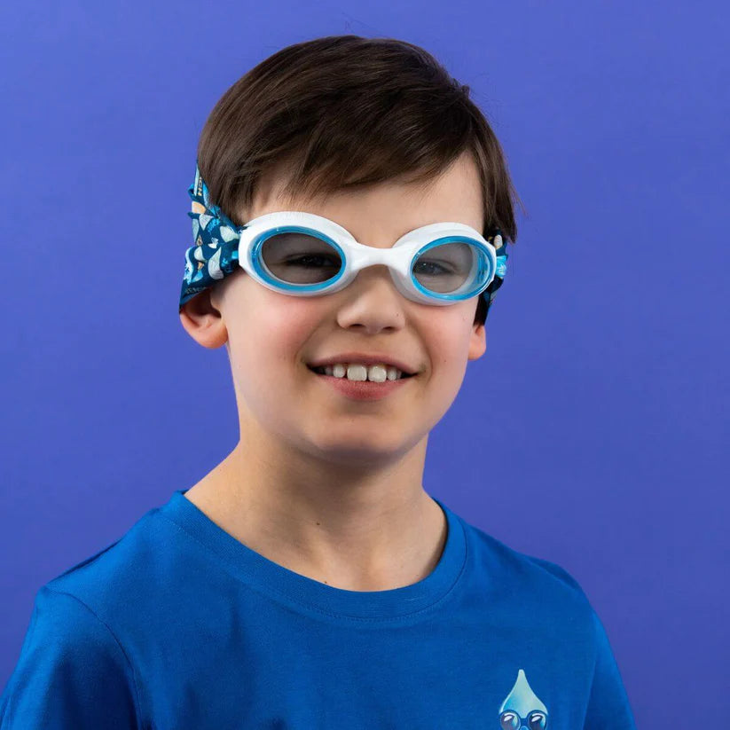 Criança sorridente a usar os Waterplops Óculos para Piscina Surf de armação branca e lentes azuis com a banda de pranchas de surf, vista frontal.
