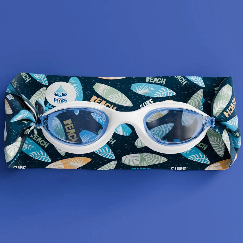 Waterplops Óculos para Piscina Surf de armação branca e lentes azuis, colocados sobre a banda elástica desdobrada com padrão de pranchas de surf, em fundo azul.