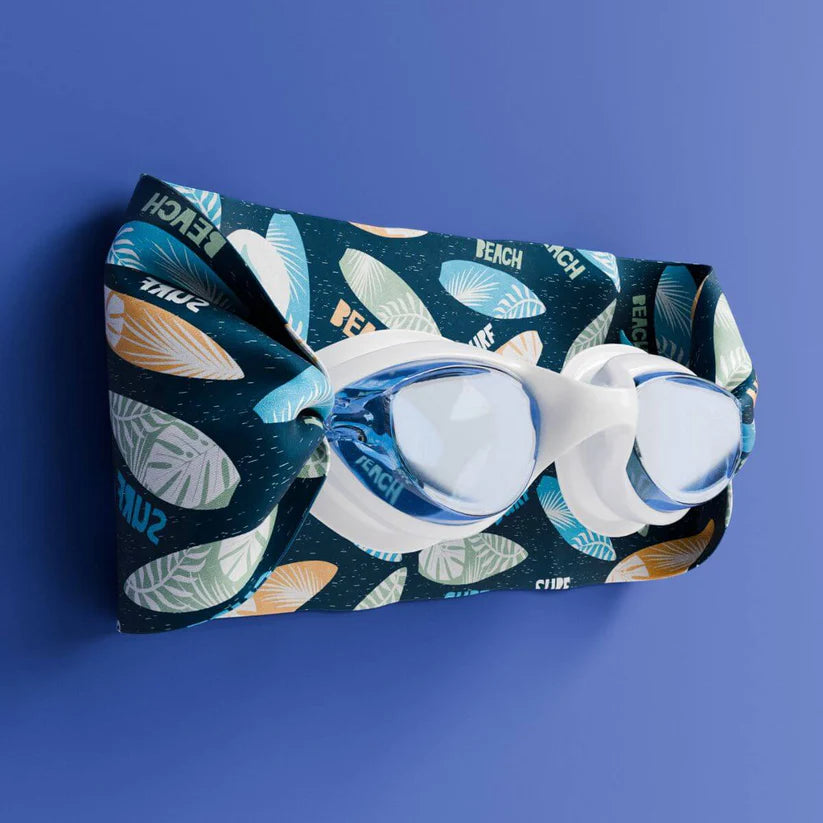 Waterplops Óculos para Piscina Surf de armação branca e lentes azuis, numa vista angular sobre a banda elástica com padrão de pranchas de surf, em fundo azul.