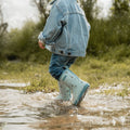 Criança a caminhar por uma superfície molhada, usando galochas Little Dutch azuis, com água a salpicar ao redor.