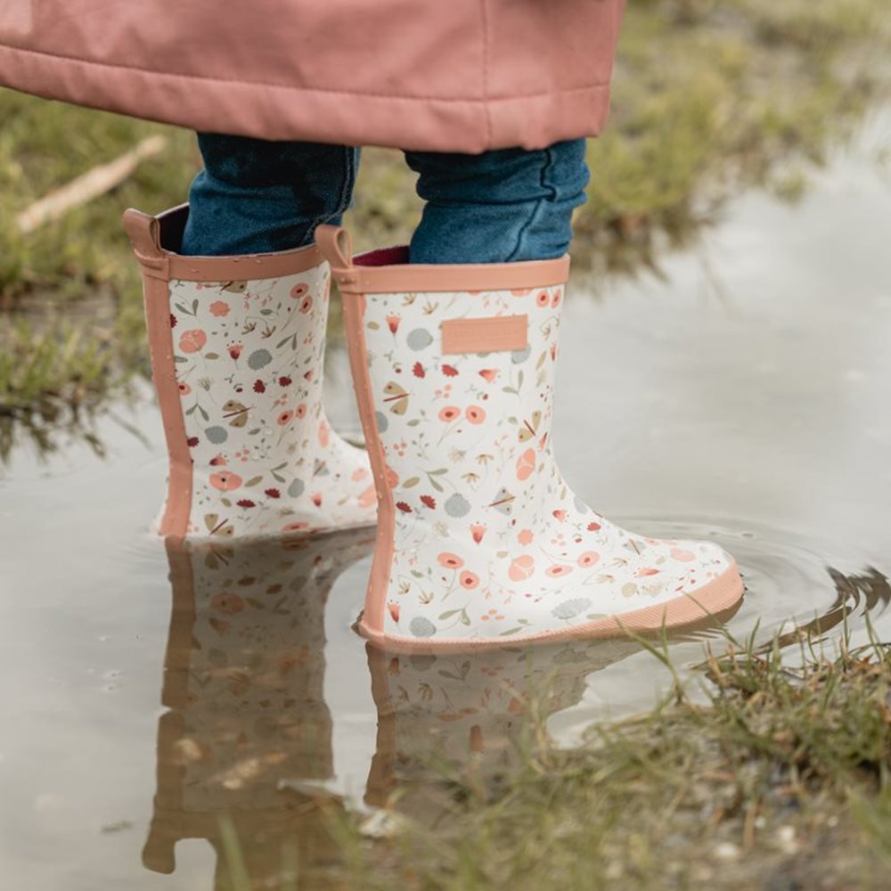 Galochas Little Dutch florais em detalhe, refletidas na água, mostrando resistência e estilo infantil.