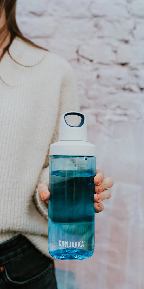 Mulher a segurar a garrafa Kambukka RENO Sapphire 500ml azul, cheia de líquido, destacando a pega e o uso prático.