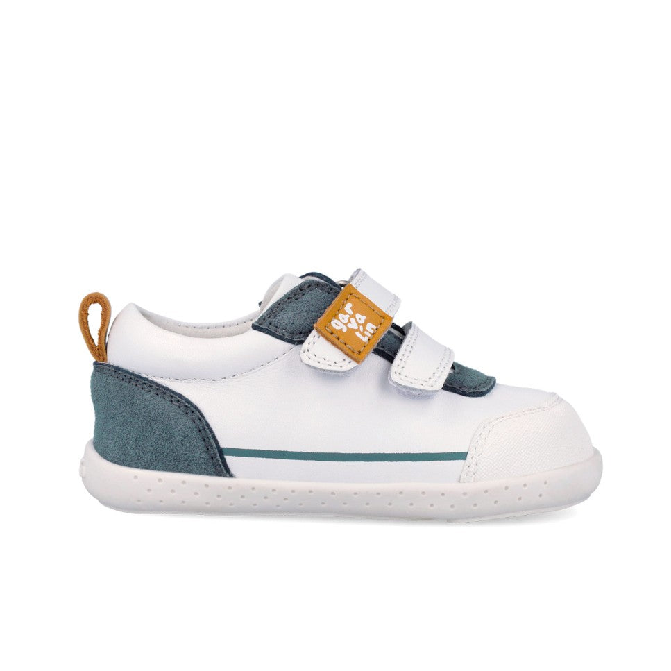 Sapatilha Garvalín para criança em branco e petrol, vista de lado, com fecho duplo de velcro e sola flexível estilo barefoot.