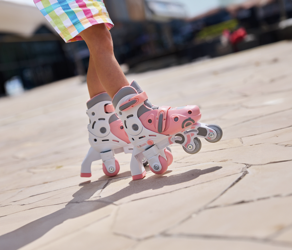 Criança a usar os patins Globber 2 em 1 rosa pastel em modo em linha sobre pavimento exterior.