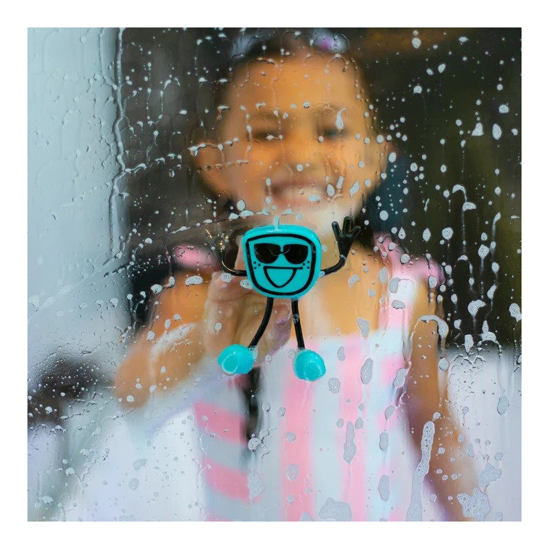 Criança sorridente a brincar com o boneco Glo Pal Alex (azul/preto) que adere a uma janela molhada e com espuma.