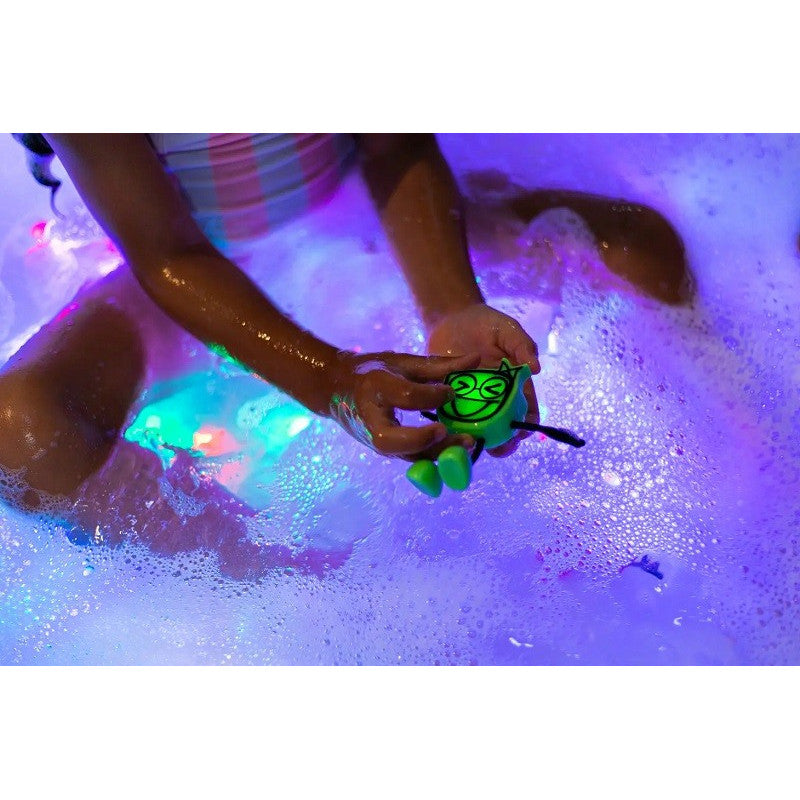 Mãos de criança seguram o boneco Glo Pal na banheira cheia de espuma e luzes LED coloridas.